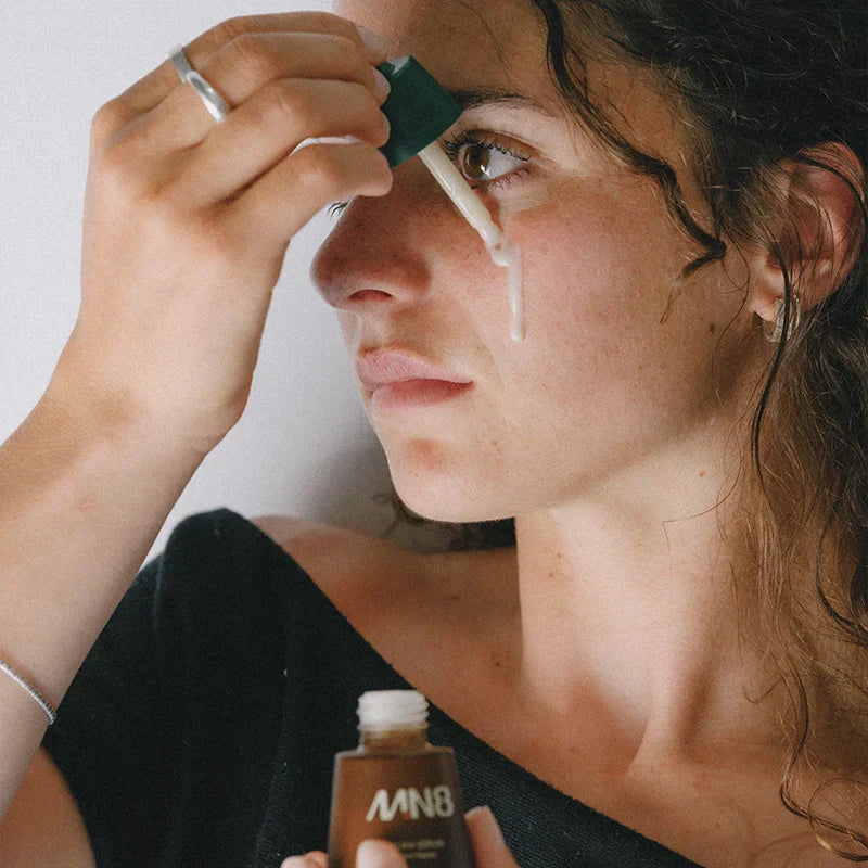 Woman applying MN8 Mānuka Repair Serum drops to face using the dropper