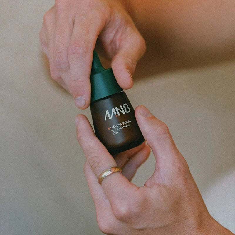Hands holding MN8 Mānuka Repair Serum 30ml dropper bottle
