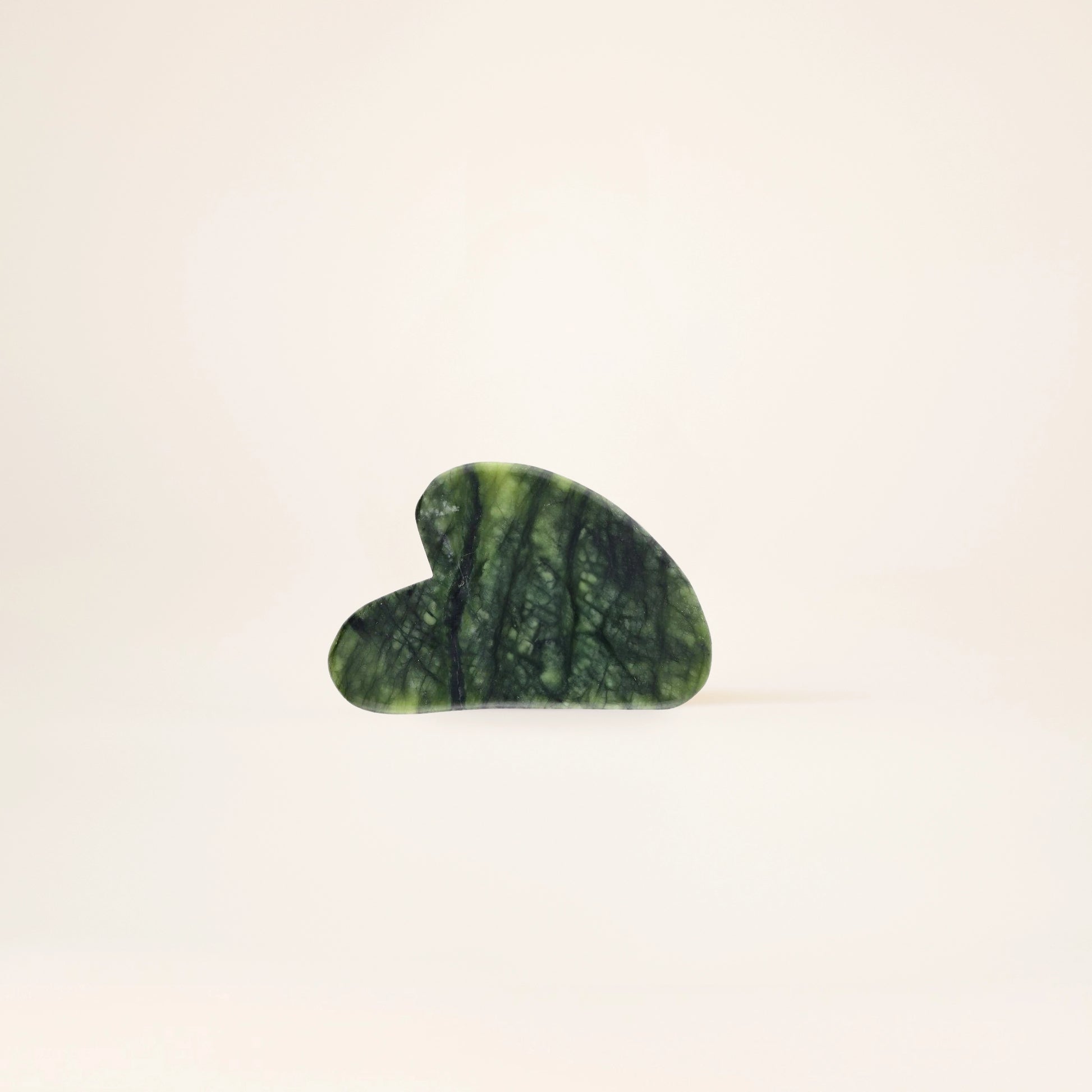 Heart-shaped green stone Gua Sha on a beige background
